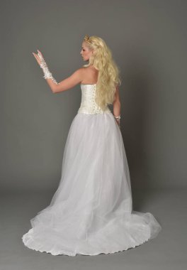 tam uzunlukta portre sarışın kız beyaz cüppe, kameranın arka ayakta pozuyla giyiyor. gri studio arka plan.