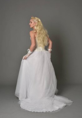 tam uzunlukta portre sarışın kız beyaz cüppe, kameranın arka ayakta pozuyla giyiyor. gri studio arka plan.