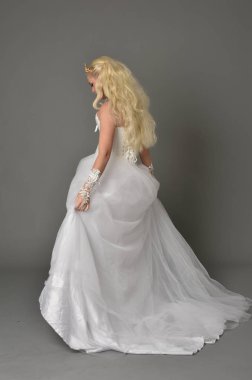 tam uzunlukta portre sarışın kız beyaz cüppe, kameranın arka ayakta pozuyla giyiyor. gri studio arka plan.