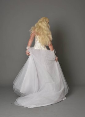 tam uzunlukta portre sarışın kız beyaz cüppe, kameranın arka ayakta pozuyla giyiyor. gri studio arka plan.