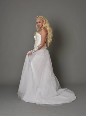 tam uzunlukta portre sarışın kız beyaz cüppe, kameranın arka ayakta pozuyla giyiyor. gri studio arka plan.