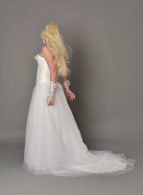 tam uzunlukta portre sarışın kız beyaz cüppe, kameranın arka ayakta pozuyla giyiyor. gri studio arka plan.