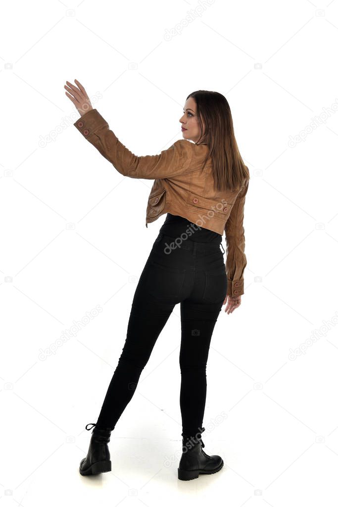 full length portrait of brunette girl wearing leather jacket and plain black clothes. standing pose, isolated on white studio background.
