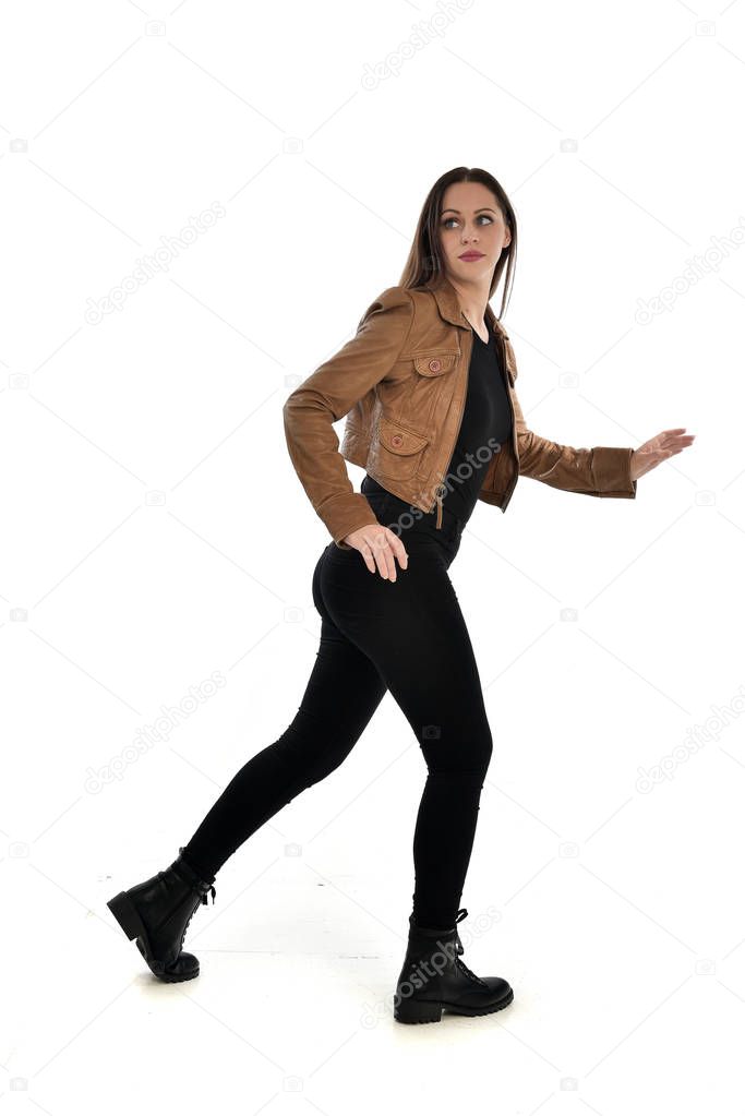 full length portrait of brunette girl wearing leather jacket and plain black clothes. standing pose, isolated on white studio background.