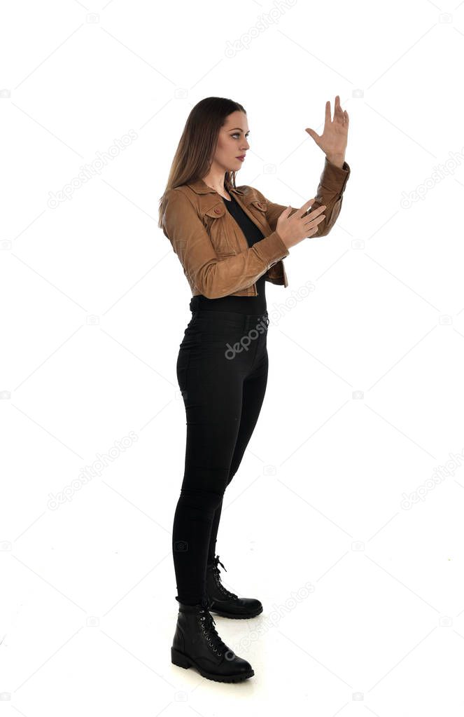 full length portrait of brunette girl wearing brown leather jacket. side profile, standing pose on white background.