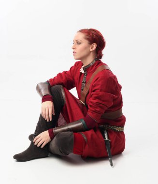 Kırmızı saçlı kız fantezi Ortaçağ giyinen, stüdyo arka plan üzerinde oturmuş poz tam uzunlukta portresi.