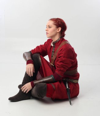 Kırmızı saçlı kız fantezi Ortaçağ giyinen, stüdyo arka plan üzerinde oturmuş poz tam uzunlukta portresi.