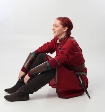 Kırmızı saçlı kız fantezi Ortaçağ giyinen, stüdyo arka plan üzerinde oturmuş poz tam uzunlukta portresi.