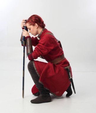 Kırmızı saçlı kız fantezi Ortaçağ giyinen, stüdyo arka plan üzerinde oturmuş poz tam uzunlukta portresi.