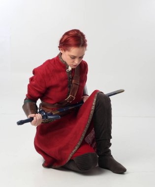 Kırmızı saçlı kız fantezi Ortaçağ giyinen, stüdyo arka plan üzerinde oturmuş poz tam uzunlukta portresi.