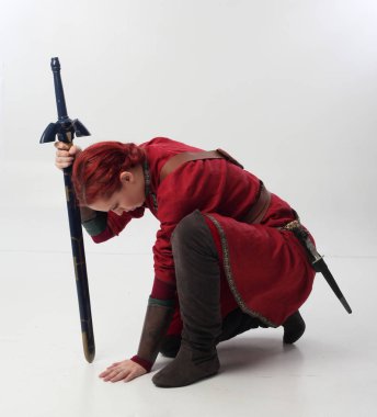 Kırmızı saçlı kız fantezi Ortaçağ giyinen, stüdyo arka plan üzerinde oturmuş poz tam uzunlukta portresi.