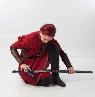 Kırmızı saçlı kız fantezi Ortaçağ giyinen, stüdyo arka plan üzerinde oturmuş poz tam uzunlukta portresi.