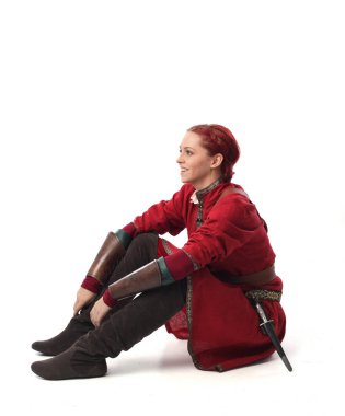 Kırmızı saçlı kız fantezi Ortaçağ giyinen, stüdyo arka plan üzerinde oturmuş poz tam uzunlukta portresi.