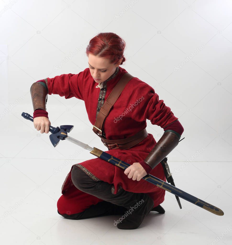 full length portrait of red haired girl wearing fantasy medieval costume, seated pose on studio background.