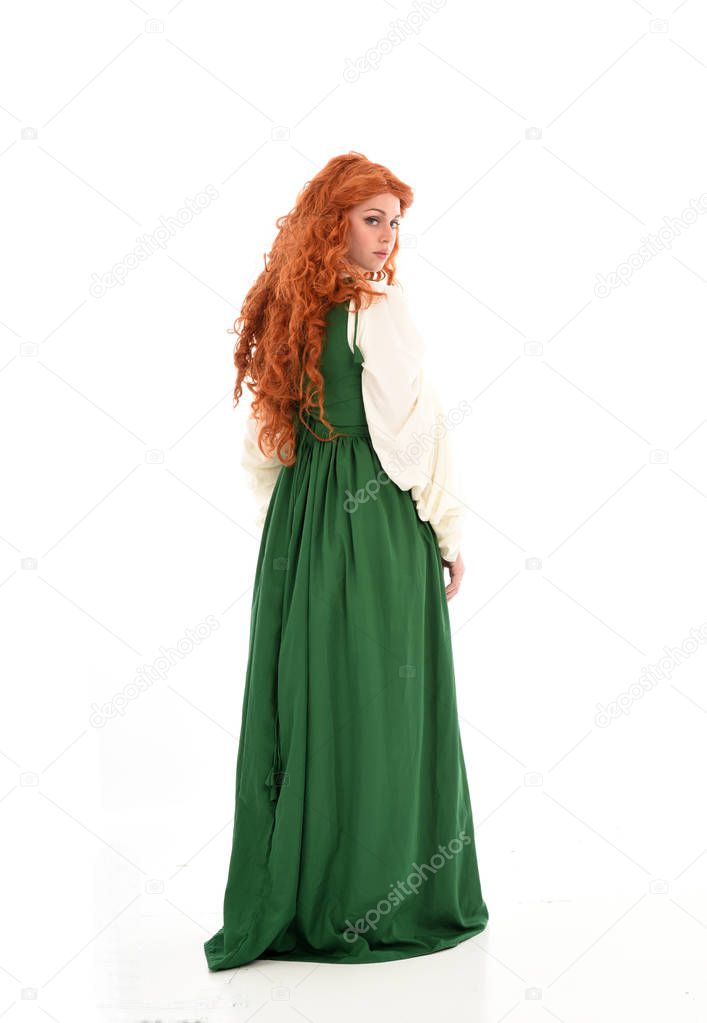 full length portrait of red haired girl wearing green medieval gown. standing pose on white studio background.