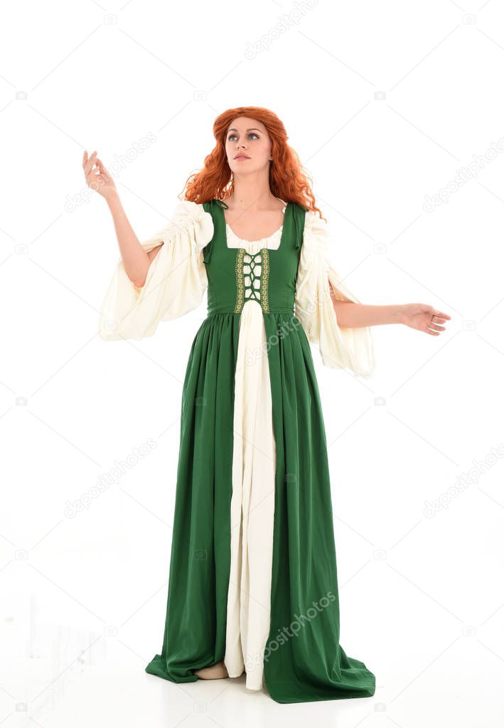full length portrait red haired girl wearing green medieval gown, standing pose. isolated on white studio background.