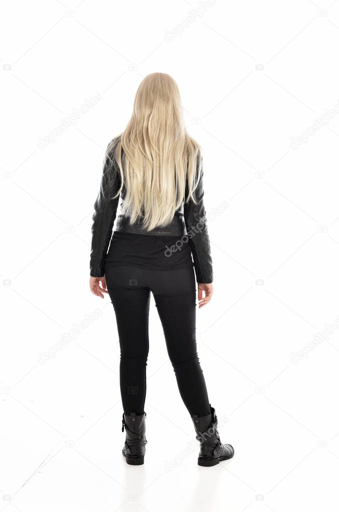 full length portrait of blonde girl wearing black leather clothes. standing pose with back to the camera. isolated on white studio background.