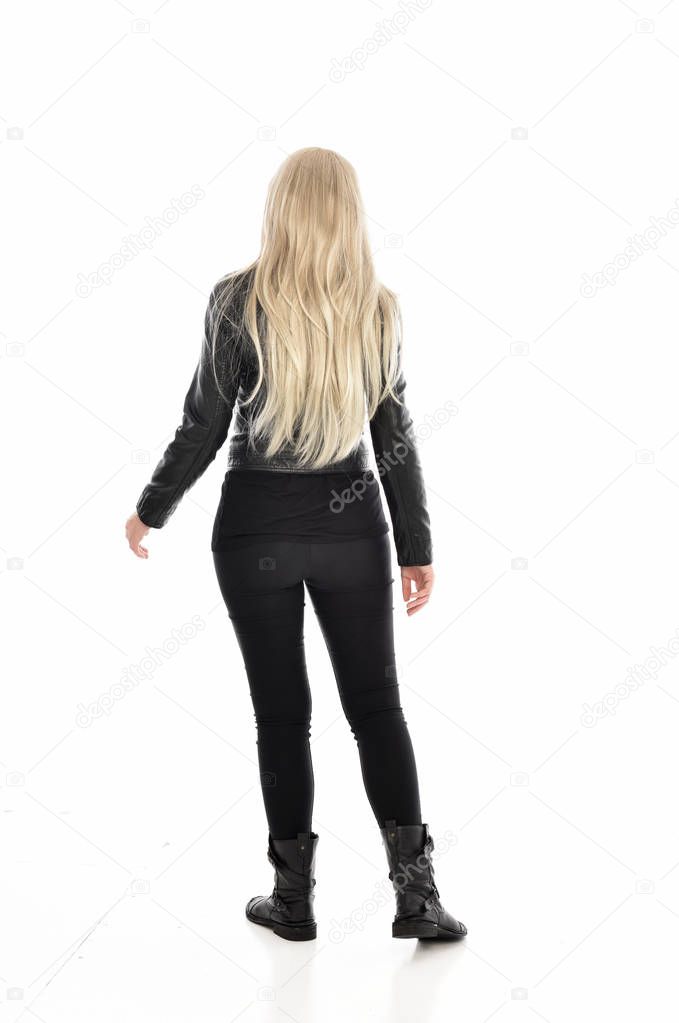 full length portrait of blonde girl wearing black leather clothes. standing pose with back to the camera. isolated on white studio background.