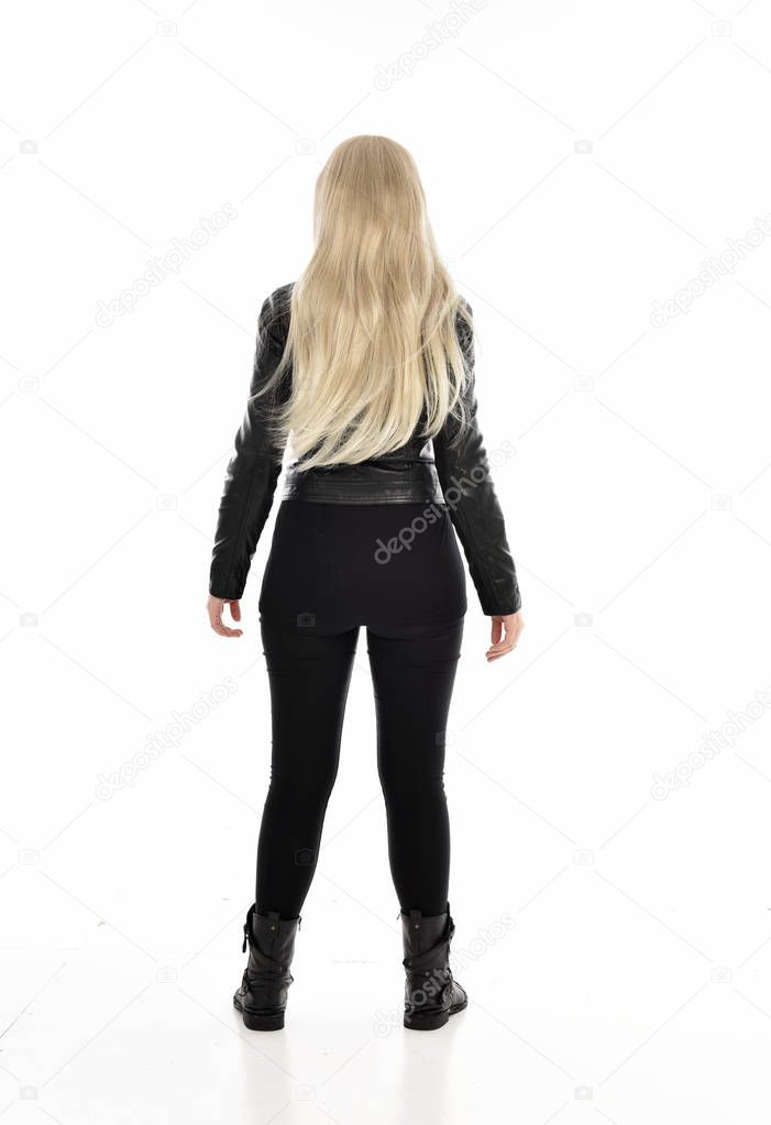 full length portrait of blonde girl wearing black leather clothes. standing pose with back to the camera. isolated on white studio background.