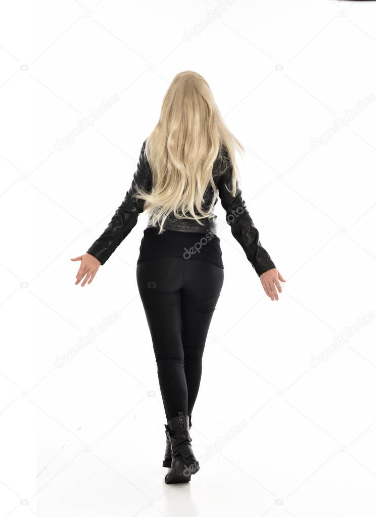 full length portrait of blonde girl wearing black leather clothes. standing pose with back to the camera. isolated on white studio background.