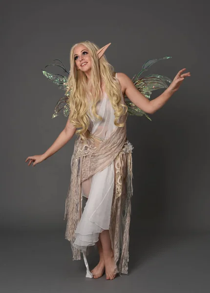 full length portrait blonde girl wearing fantasy fairy costume, standing pose. grey studio background.