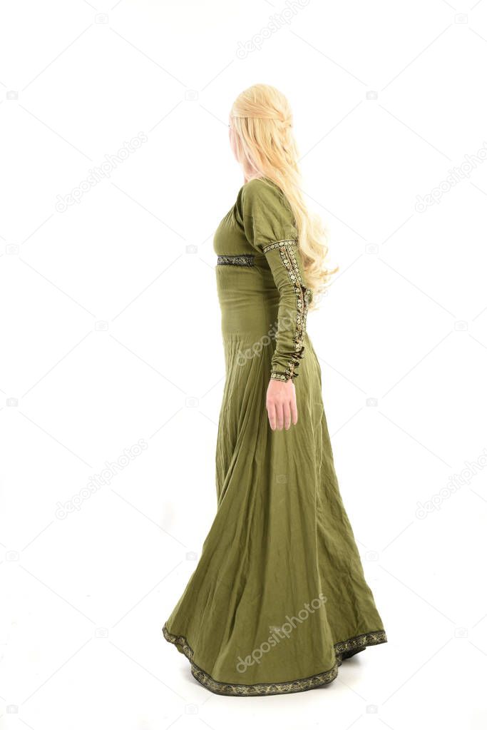 full length portrait of blonde girl wearing green medieval gown. standing pose facing away from the camera, isolated on white studio background.