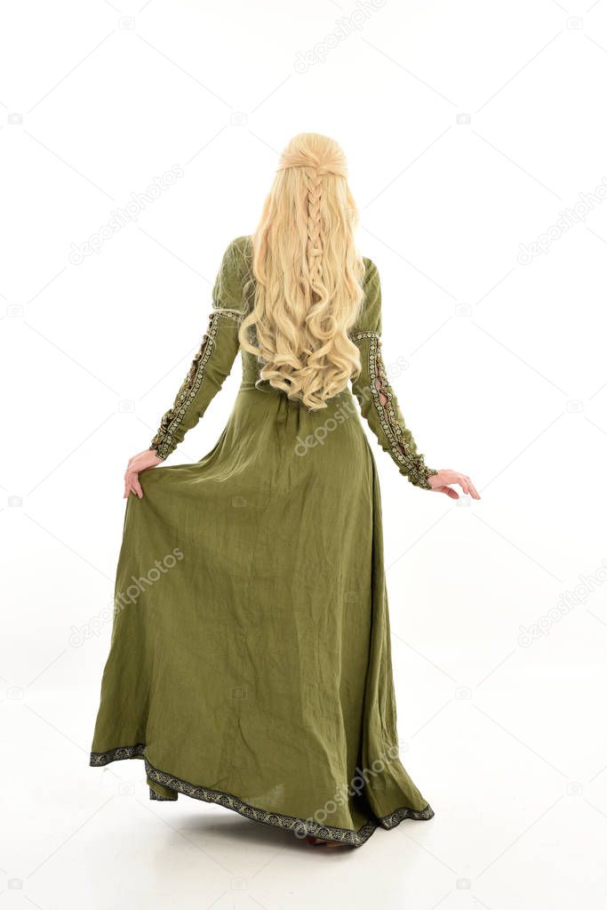 full length portrait of blonde girl wearing green medieval gown. standing pose facing away from the camera, isolated on white studio background.