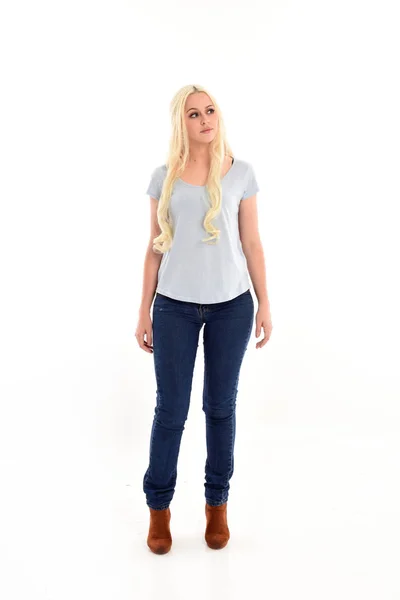 ホワイト スタジオの背景に分離されたポーズを立っている青いシャツとジーンズを身に着けているブロンドの女の子の完全な長さの肖像画 — ストック写真