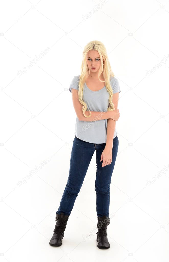full length portrait of blonde girl wearing blue shirt and jeans, standing pose isolated on white studio background.