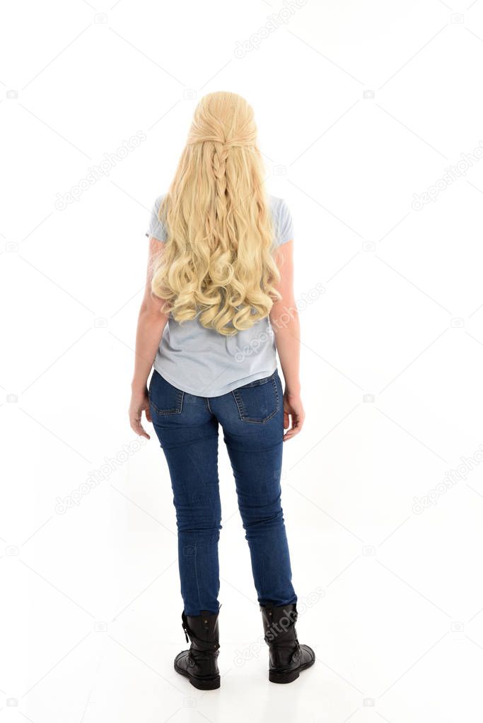 full length portrait of a blonde girl wearing casual blue shirt and jeans,. standing pose, facing away from the camera. isolated on white studio background.