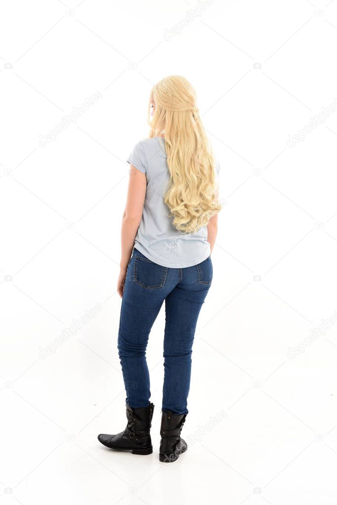 full length portrait of a blonde girl wearing casual blue shirt and jeans,. standing pose, facing away from the camera. isolated on white studio background.