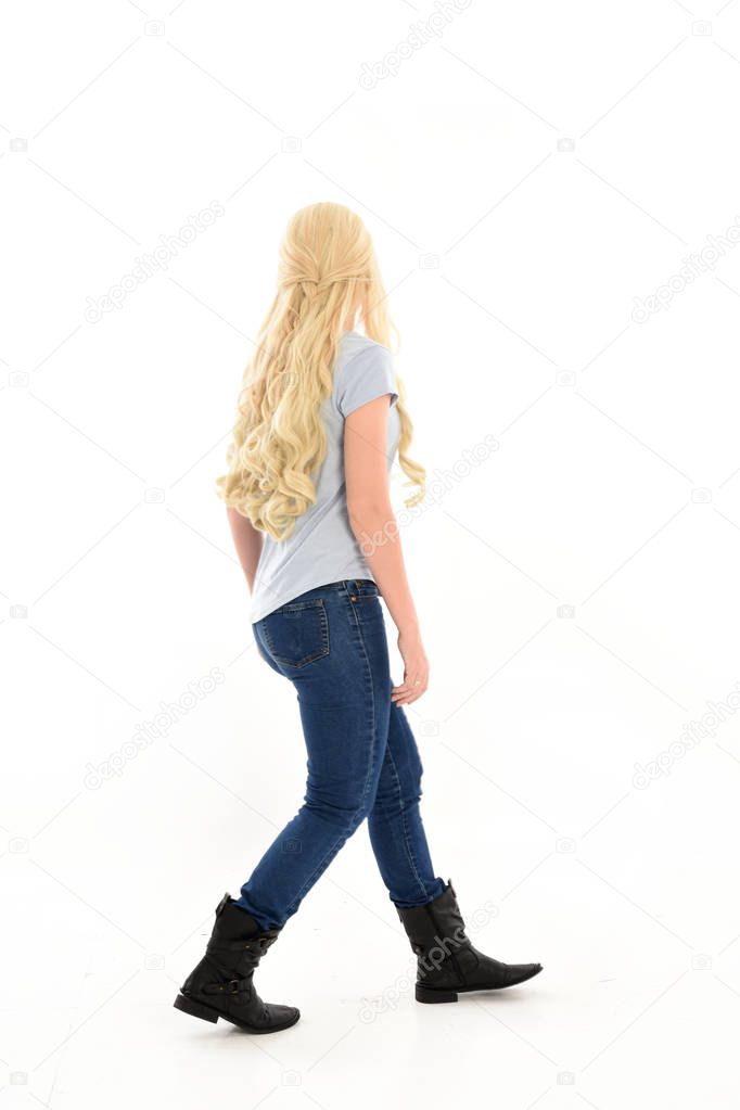 full length portrait of a blonde girl wearing casual blue shirt and jeans,. standing pose, facing away from the camera. isolated on white studio background.