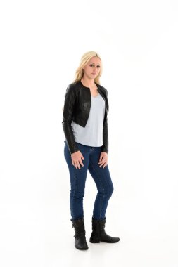 full length portrait o blonde girl wearing leather jacket and jeans. standing pose, isolated against white studio background.