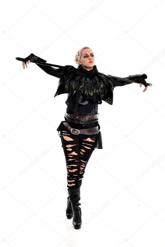 full length portrait of blonde girl wearing black torn outfit, holding a staff weapon. standing pose, isolated on white studio background.