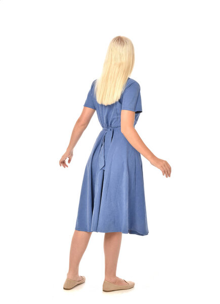full length portrait of blonde girl wearing blue dress. standing pose with back to the camera. isolated on white  studio background.