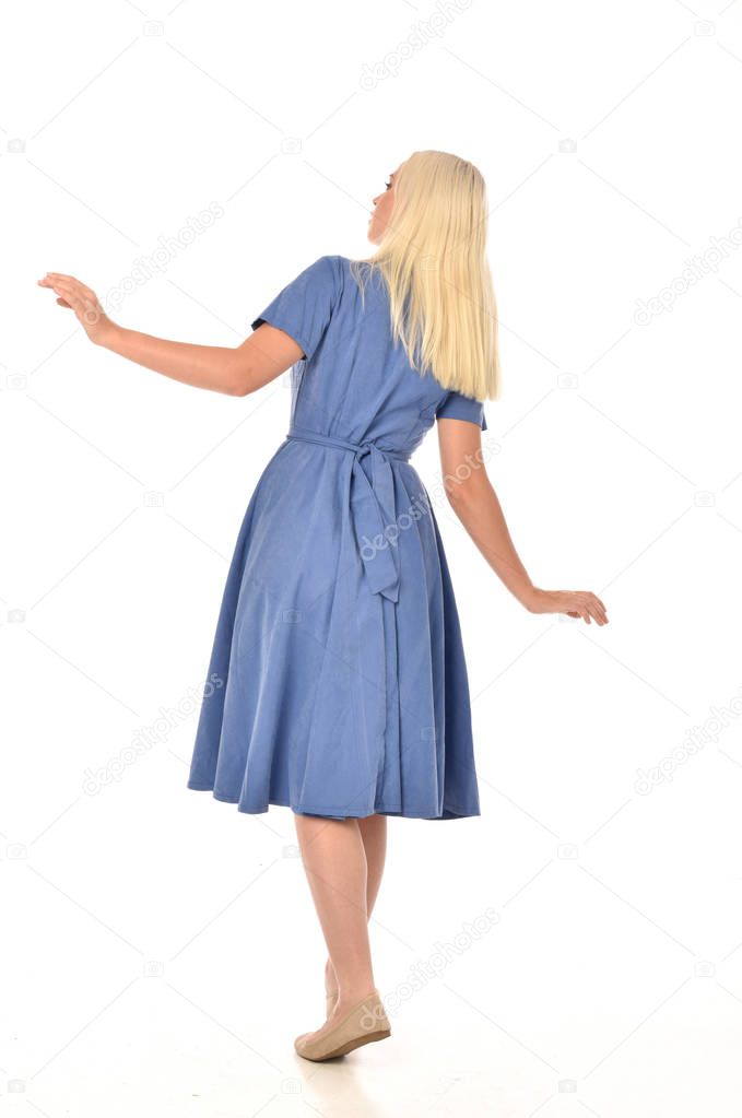 full length portrait of blonde girl wearing blue dress. standing pose with back to the camera. isolated on white  studio background.