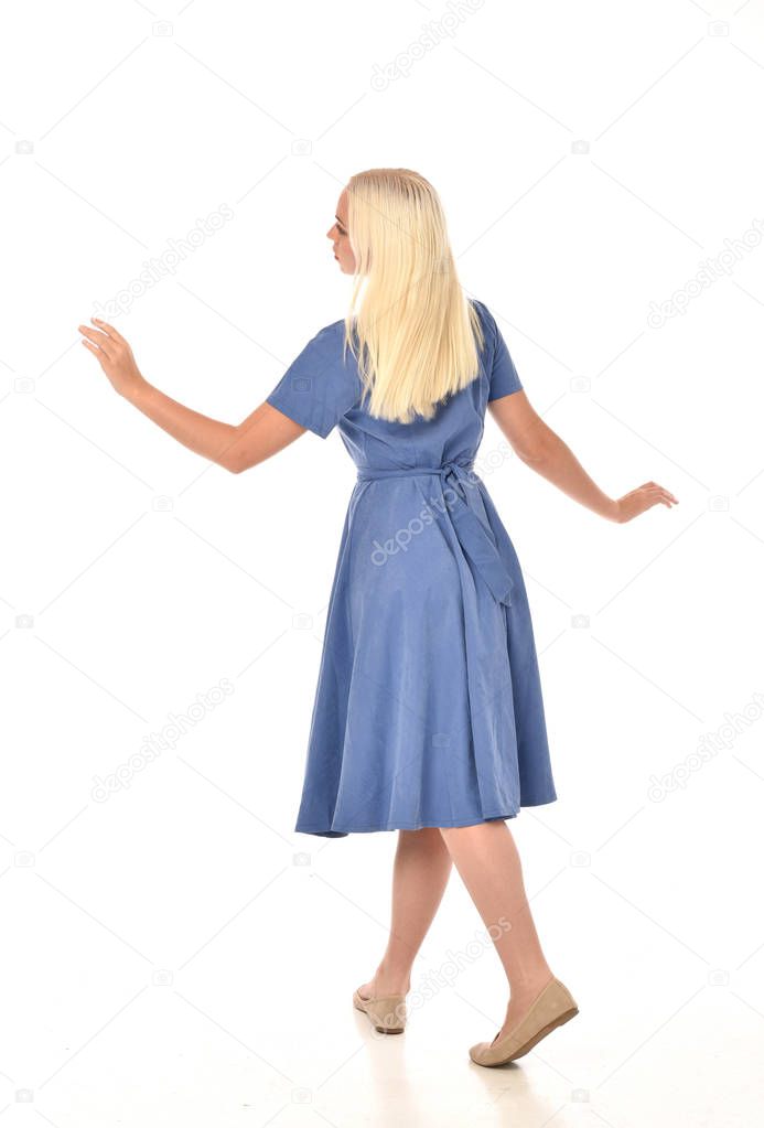 full length portrait of blonde girl wearing blue dress. standing pose with back to the camera. isolated on white  studio background.
