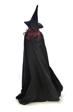 full length portrait of red haired girl wearing long black cloak, pointy hat and witch costume. standing pose, isolated on white studio background. clipart