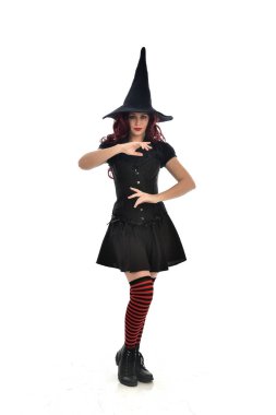 tam uzunlukta portresi kırmızı saçlı kız kara cadı kostüm ve sivri şapka giyiyor. ayakta poz, beyaz stüdyo arka plan üzerinde izole.