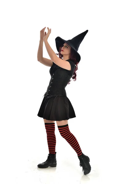 身穿黑色女巫服装和尖帽的红头发女孩全长肖像 站立的姿态 被隔绝在白色演播室背景 — 图库照片