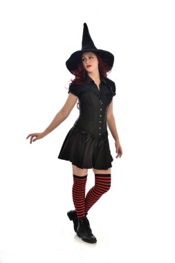 tam uzunlukta portresi kırmızı saçlı kız kara cadı kostüm ve sivri şapka giyiyor. ayakta poz, beyaz stüdyo arka plan üzerinde izole.