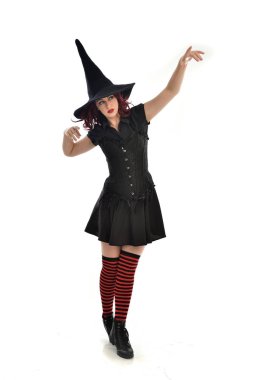 tam uzunlukta portresi kırmızı saçlı kız kara cadı kostüm ve sivri şapka giyiyor. ayakta poz, beyaz stüdyo arka plan üzerinde izole.