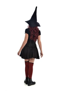 tam uzunlukta portresi kırmızı saçlı kız kara cadı kostüm ve sivri şapka giyiyor. arka beyaz stüdyo arka plan üzerinde izole kamera ile ayakta poz.