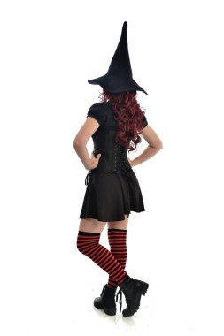 tam uzunlukta portresi kırmızı saçlı kız kara cadı kostüm ve sivri şapka giyiyor. arka beyaz stüdyo arka plan üzerinde izole kamera ile ayakta poz.