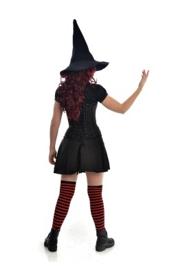 tam uzunlukta portresi kırmızı saçlı kız kara cadı kostüm ve sivri şapka giyiyor. arka beyaz stüdyo arka plan üzerinde izole kamera ile ayakta poz.