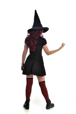 tam uzunlukta portresi kırmızı saçlı kız kara cadı kostüm ve sivri şapka giyiyor. arka beyaz stüdyo arka plan üzerinde izole kamera ile ayakta poz.