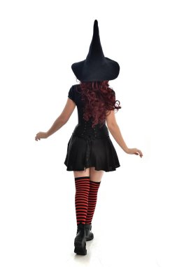tam uzunlukta portresi kırmızı saçlı kız kara cadı kostüm ve sivri şapka giyiyor. arka beyaz stüdyo arka plan üzerinde izole kamera ile ayakta poz.