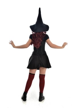 tam uzunlukta portresi kırmızı saçlı kız kara cadı kostüm ve sivri şapka giyiyor. arka beyaz stüdyo arka plan üzerinde izole kamera ile ayakta poz.