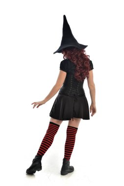 tam uzunlukta portresi kırmızı saçlı kız kara cadı kostüm ve sivri şapka giyiyor. arka beyaz stüdyo arka plan üzerinde izole kamera ile ayakta poz.