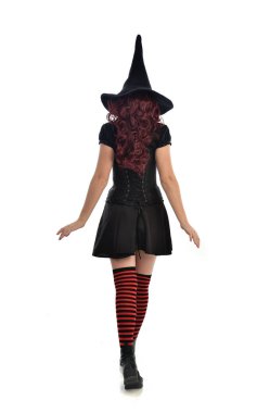 tam uzunlukta portresi kırmızı saçlı kız kara cadı kostüm ve sivri şapka giyiyor. arka beyaz stüdyo arka plan üzerinde izole kamera ile ayakta poz.